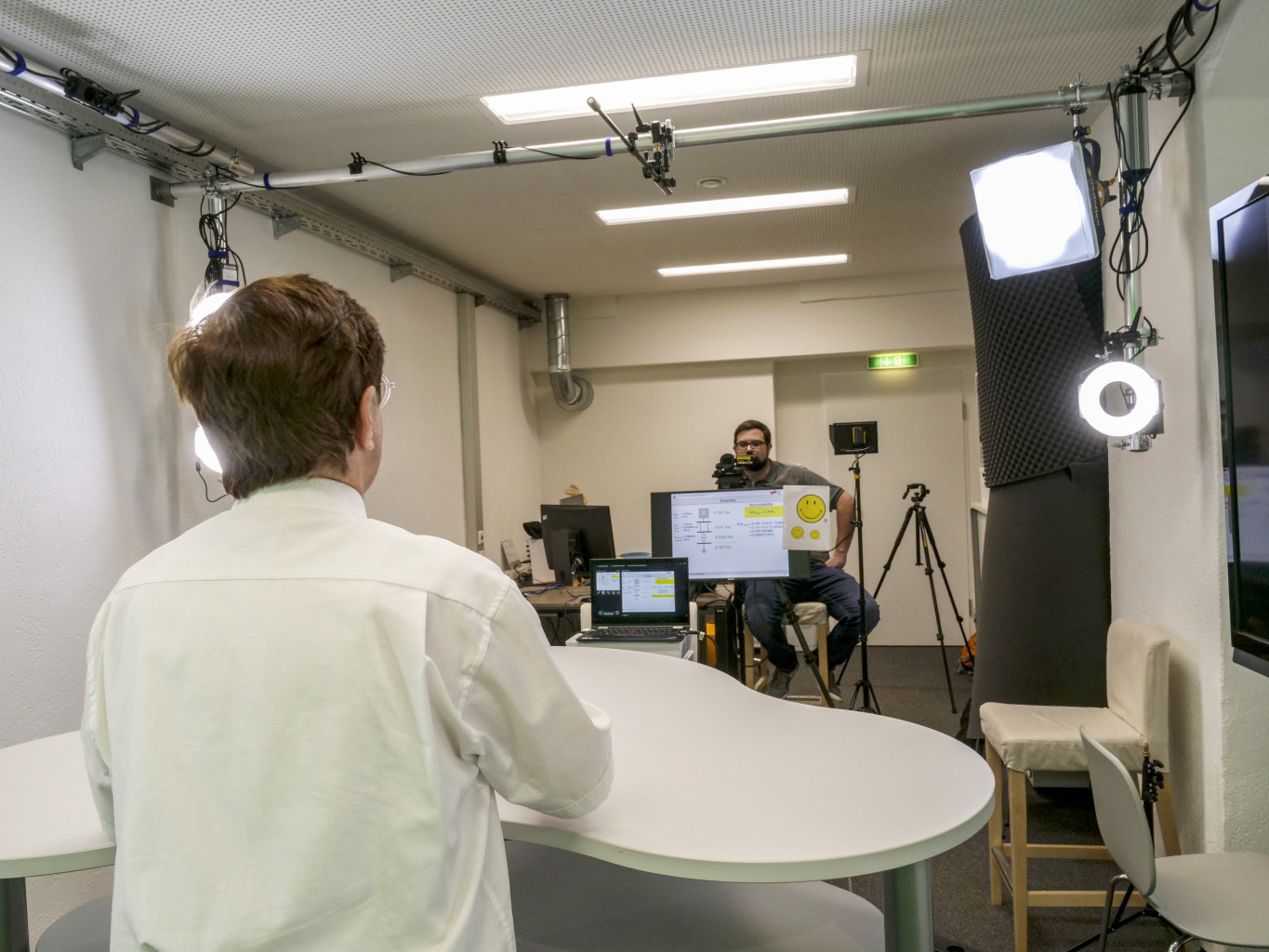 View of the person being recorded: They look at a camera and a teleprompter, and there is a support person present.