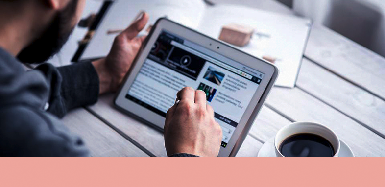 TC_Titelbild_03 ein Mann, der an einem Tisch sitzt und ein Tablet bedient. Am Tisch sind eine Tasse Kaffee und ein Buch.